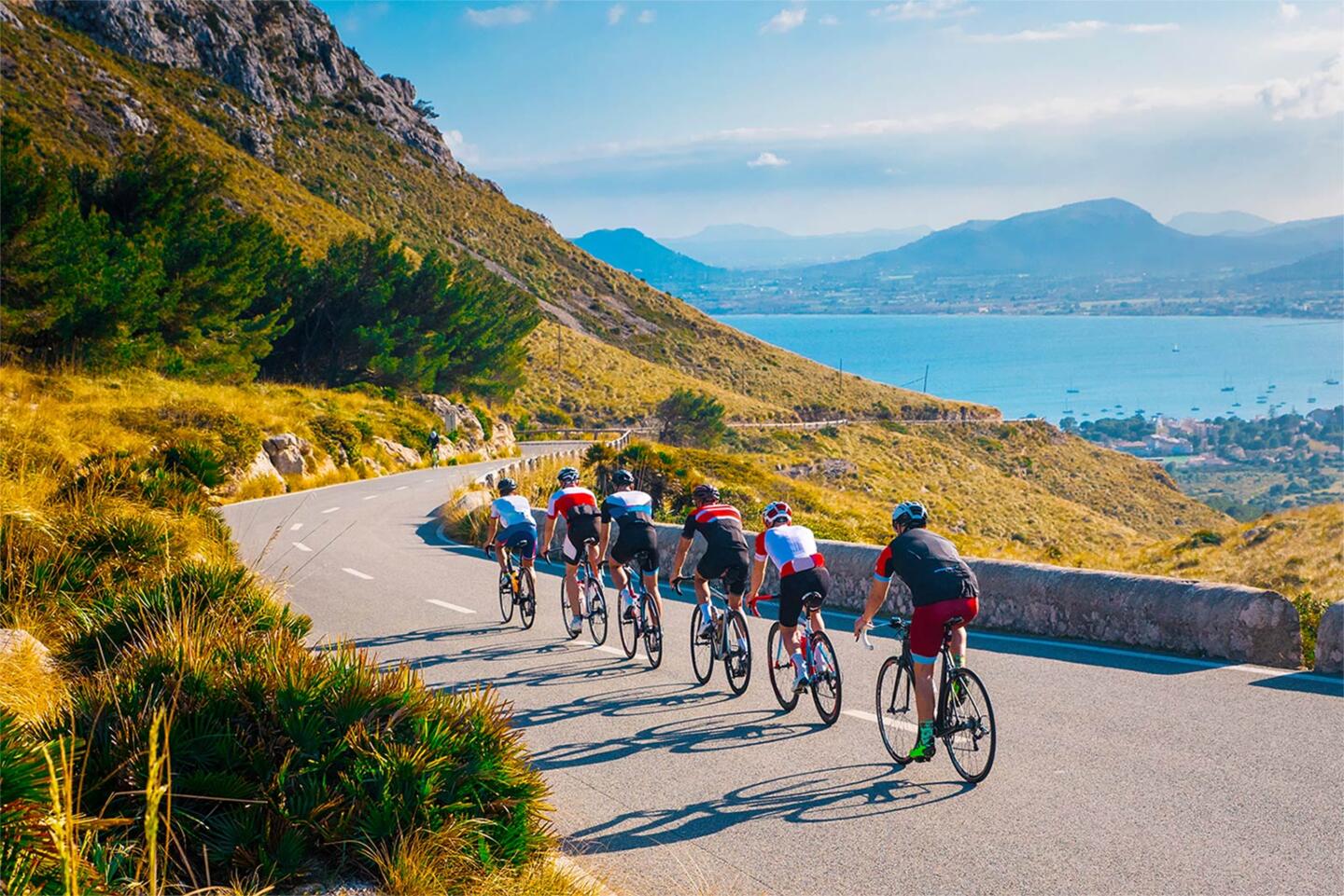Competitive cyclists on a winding mountain road during the Tour de France, with a stunning view of the bay below and the surrounding nature, experience the Tour de France by staying at Appart'City, the ideal accommodation for cycling fans.