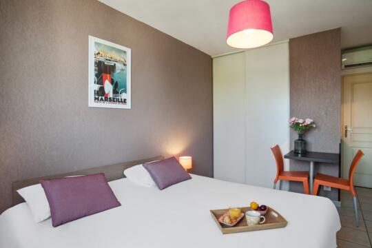 Modern and comfortable hotel room in Marseille with decorative poster, welcome tray with pastries, perfect for relaxation and business stays.