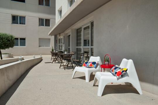 Terrasse ensoleillée de l'Appart'CIty Classic Marseille Aéroport Vitrolles, avec mobilier de jardin et jouets pour enfants, invitant à la détente en famille.