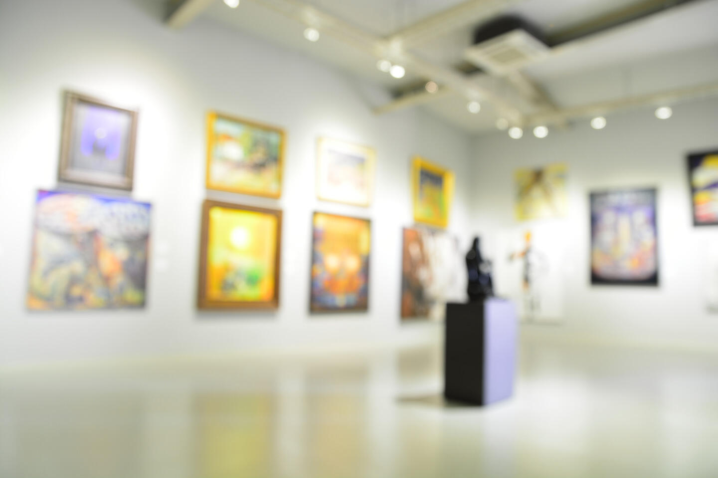 Vue intérieure floue d'une galerie d'art contemporain avec des murs ornés de tableaux colorés dans des cadres variés et une sculpture sur piédestal au centre, créant une atmosphère artistique immersive et dynamique.