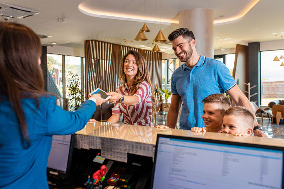 Famille souriante à la réception d’un appart’hôtel Appart’City, recevant les clés de leur chambre, représentant une offre CSE pour un séjour en famille