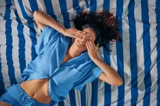 Cliente détendue allongée sur un lit rayé bleu et blanc, profitant d’un moment de confort et de relaxation.