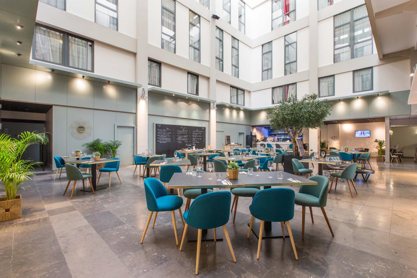 Vue intérieure du Restaurant Bistrot City Lyon Part-Dieu, décoration contemporaine avec des chaises en tissu bleu canard, tables en bois, et plantes vertes, ambiance lumineuse et accueillante.