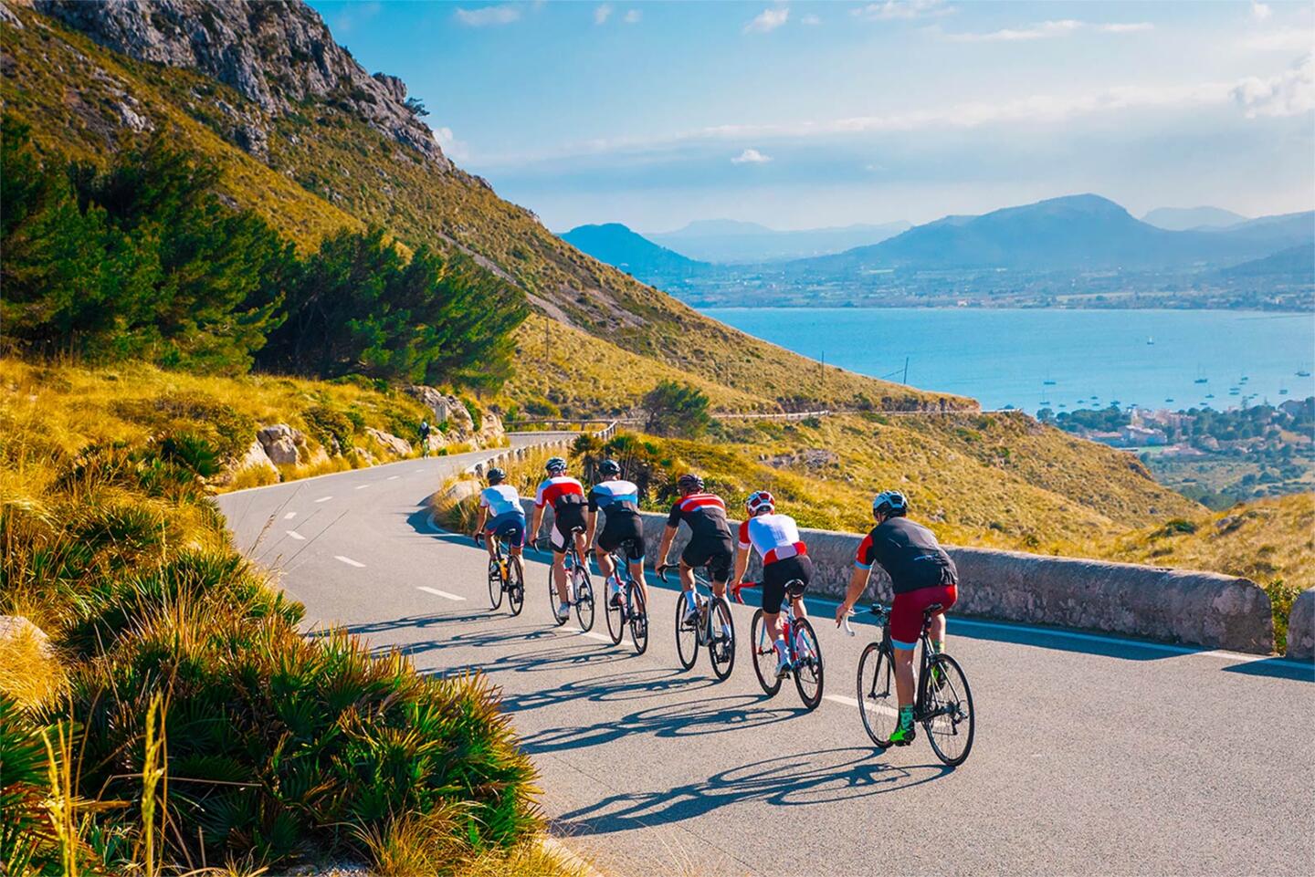 Ciclistas en competición en una carretera de montaña serpenteante durante el Tour de France, con una vista impresionante de la bahía abajo y la naturaleza circundante, vive la experiencia del Tour de France alojándote en Appart'City, el alojamiento ideal para aficionados al ciclismo.