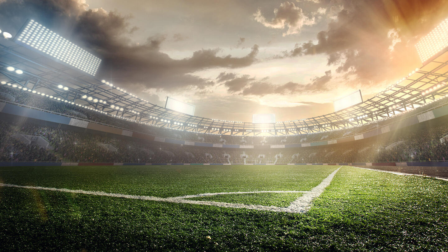 View of a lively soccer stadium with the sun setting in the background, creating a dramatic sky above the lush green lawn, illustrating the atmosphere of a match day, ideal for sports fans staying in Parisian aparthotels.