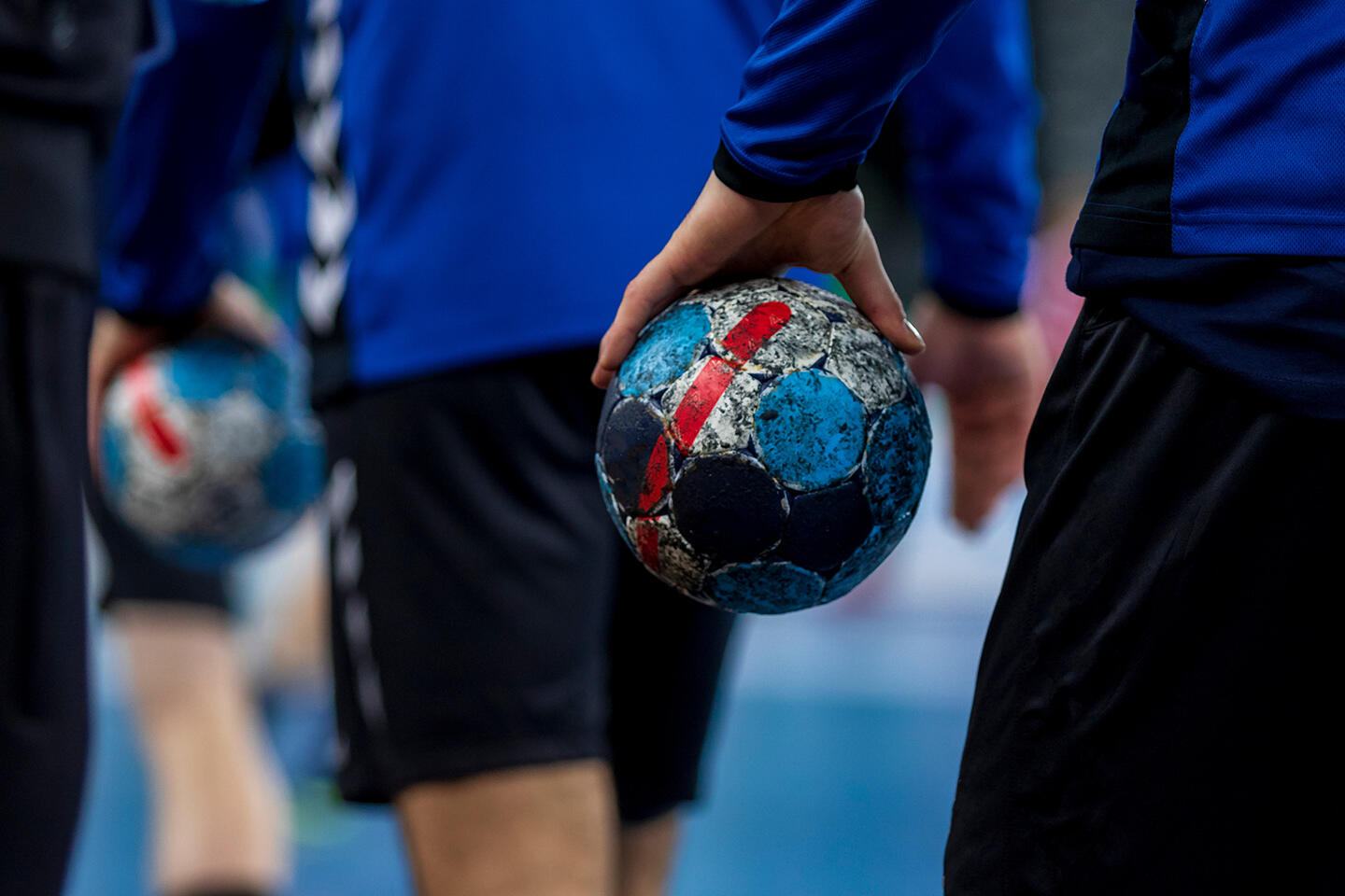 Handball players in action holding well-worn handball balls with peeling colors, symbolizing the intensity and passion of the sport, a captivating activity for guests staying in aparthotels near the Pierre-Mauroy Stadium in Lille.