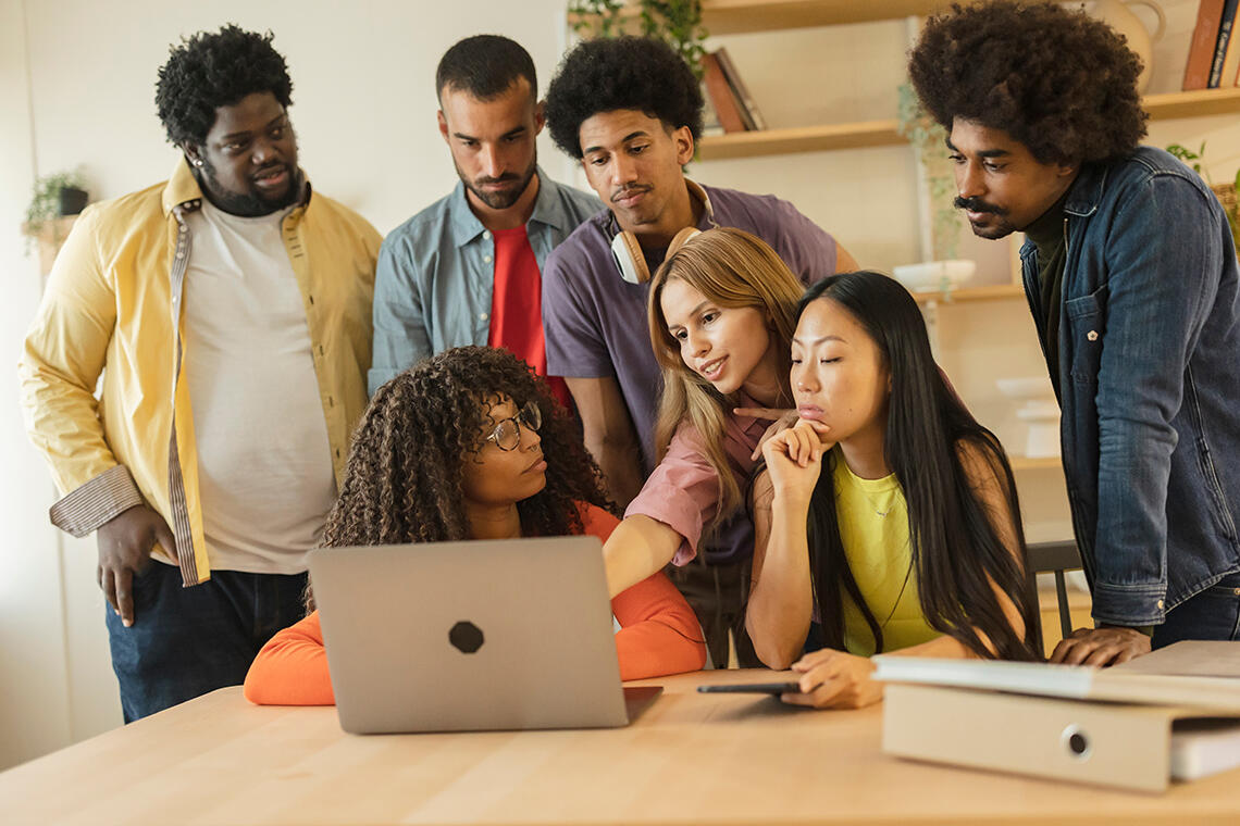 Group of young professionals engaged in teamwork at the Apprenticeship, Work-Study, and Careers Fair, closely examining content on a laptop in a bright office environment.