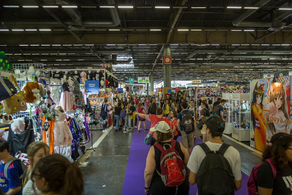 Visiteurs parcourant les stands colorés à la Japan Expo à Paris, avec des cosplays et produits de la culture pop japonaise en exposition.