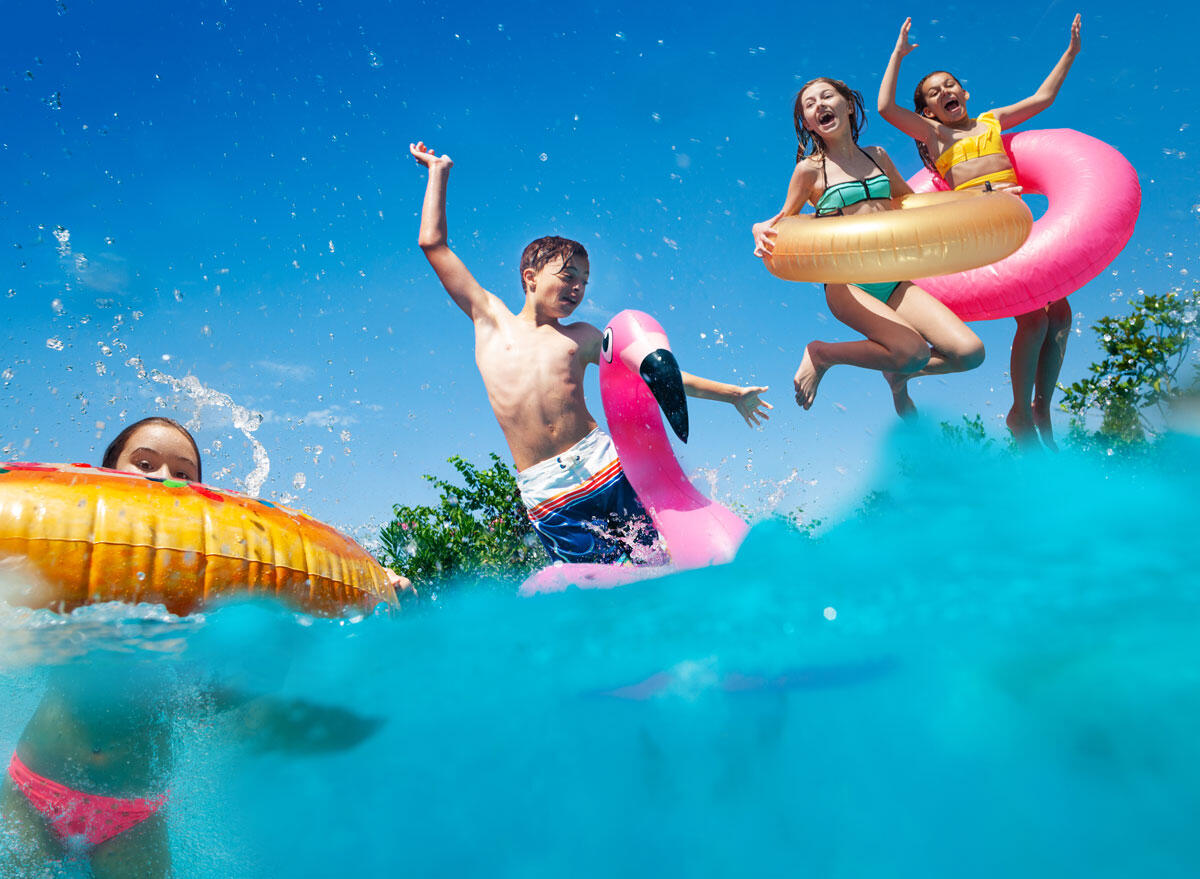 Fröhlich spielende Kinder im Pool eines Aparthotels mit bunten Schwimmreifen unter einem blauen Sommerhimmel.