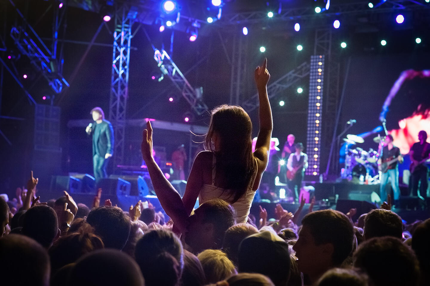 Espectador entusiasta a hombros de un festivalero en el festival Francofolies de La Rochelle, con el escenario del concierto al fondo.