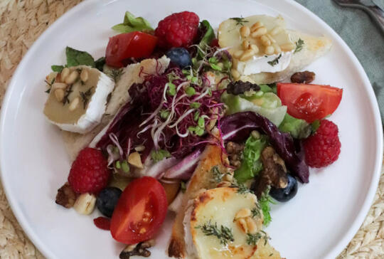 Plato gourmet saludable y colorido con ensalada fresca, queso de cabra con hierbas y piñones, tomates cherry, bayas rojas y azules, brotes de espinaca y nueces.