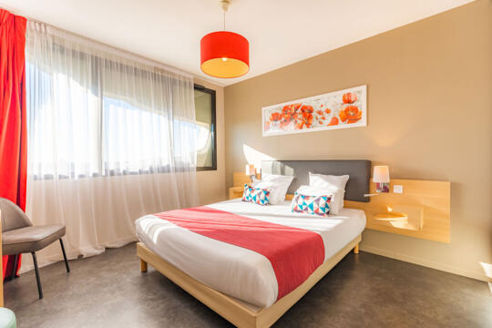 Bright and colorful Appart'City room with a comfortable double bed, floral decor, and modern touches, perfect for a relaxing stay or business trip.