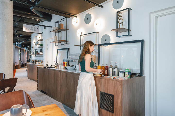 Eine elegante Frau serviert sich ein Frühstück in der modernen, gut beleuchteten Essecke eines Pariser Aparthotels mit Designereinrichtung und einladender Atmosphäre.