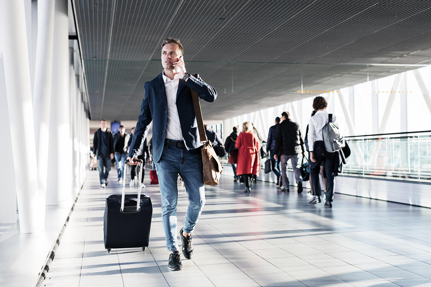 Geschäftsmann spricht am Telefon, während er mit seinem Koffer im Flughafen Brest Bretagne geht