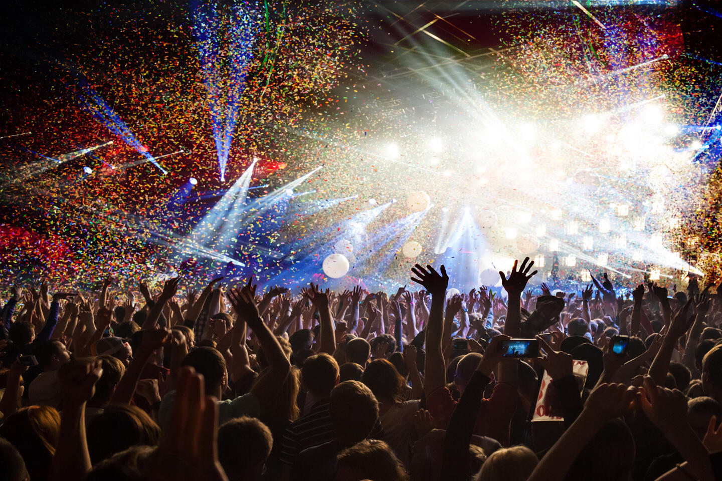 Exhilarated crowd at the Solidays festival under a shower of multicolored confetti, with spectacular light shows and an intense party atmosphere.