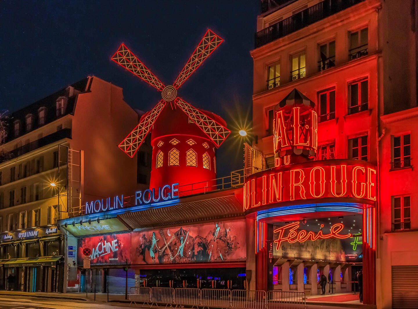 Illuminated facade of the Moulin Rouge in Paris at night with its iconic red windmill.