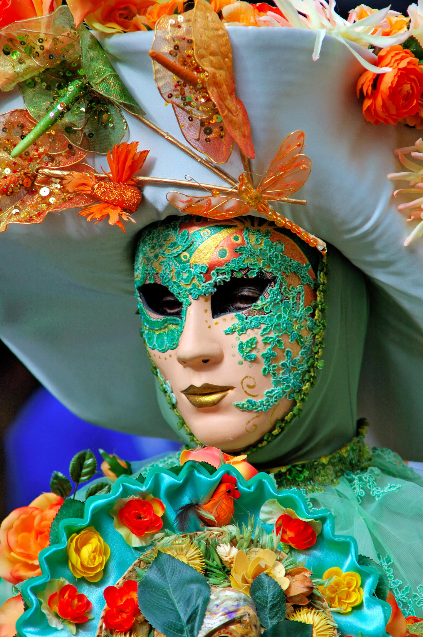 Participant avec un masque orné vert et or décoré de paillettes et de décorations florales à La Fête des Vendanges de Montmartre.