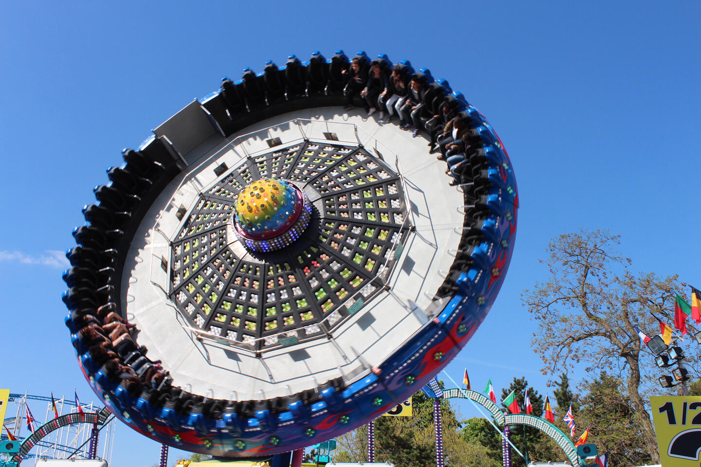 Manège tournant à la Foire du Trône avec des personnes assises autour, ciel bleu en arrière-plan