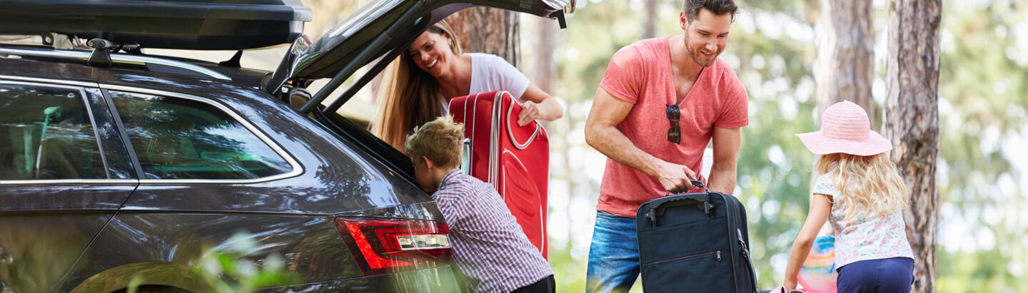 Famille chargeant des bagages dans le coffre d'une voiture en pleine nature, parfaite pour un appart hôtel à proximité des sorties d'autoroutes
