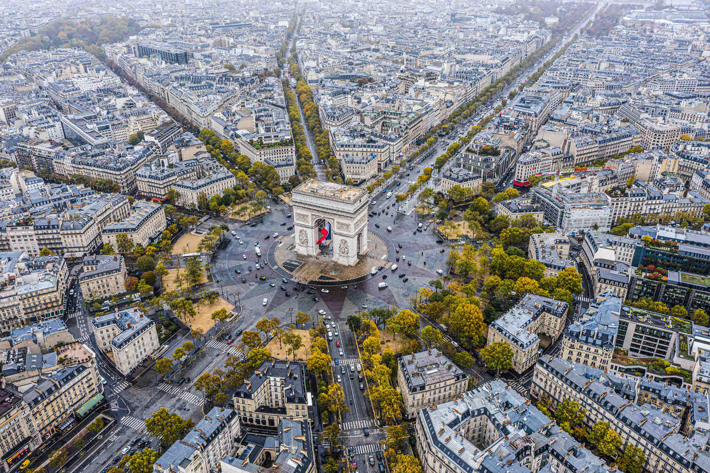 Vue aérienne de l'Arc de Triomphe au centre d'un rond-point entouré de bâtiments et d'avenues à Paris, dans le quartier des Champs-Élysées.
