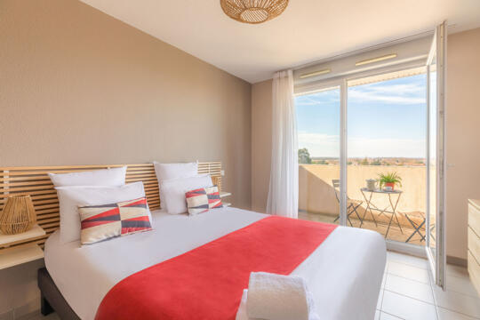Bright room with double bed, red and white bed linen, balcony view, ideal for a relaxing stay.