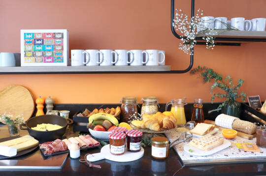 Buffet de petit déjeuner varié dans un appart'hôtel de la gamme Confort, comprenant croissants, fruits, confitures, fromages et jus de fruits.