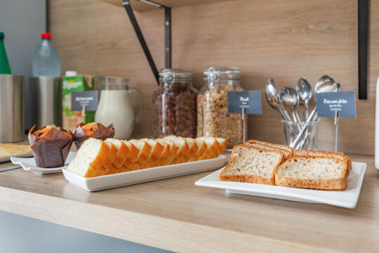 Sélection de petit déjeuner dans un appart'hôtel de la gamme Classic, avec pain tranché, muffins, céréales et lait.