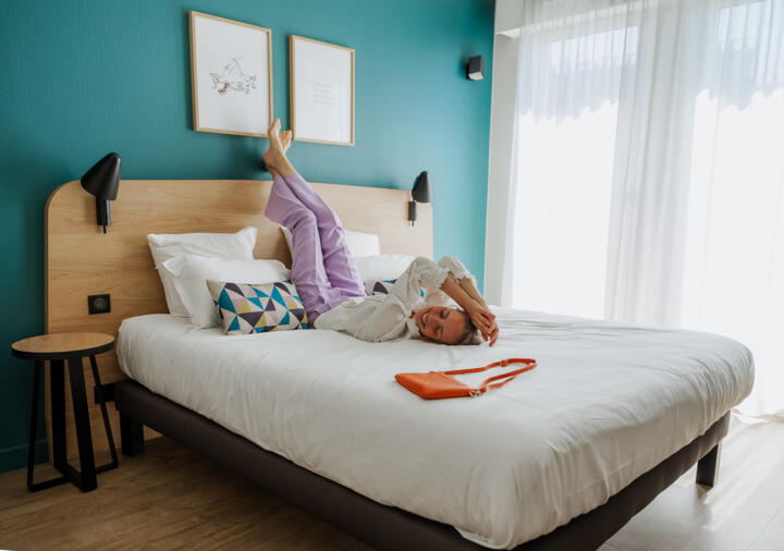 Relaxed woman lying on a bed in a modern and bright room at the aparthotel Appart'City Mairie Clichy, ideally located near Paris La Défense.
