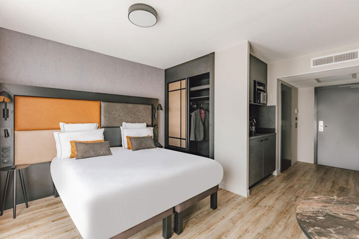 Habitación de hotel moderna con una cama doble grande, armario abierto y cocina americana en el barrio de los Campos Elíseos en París.