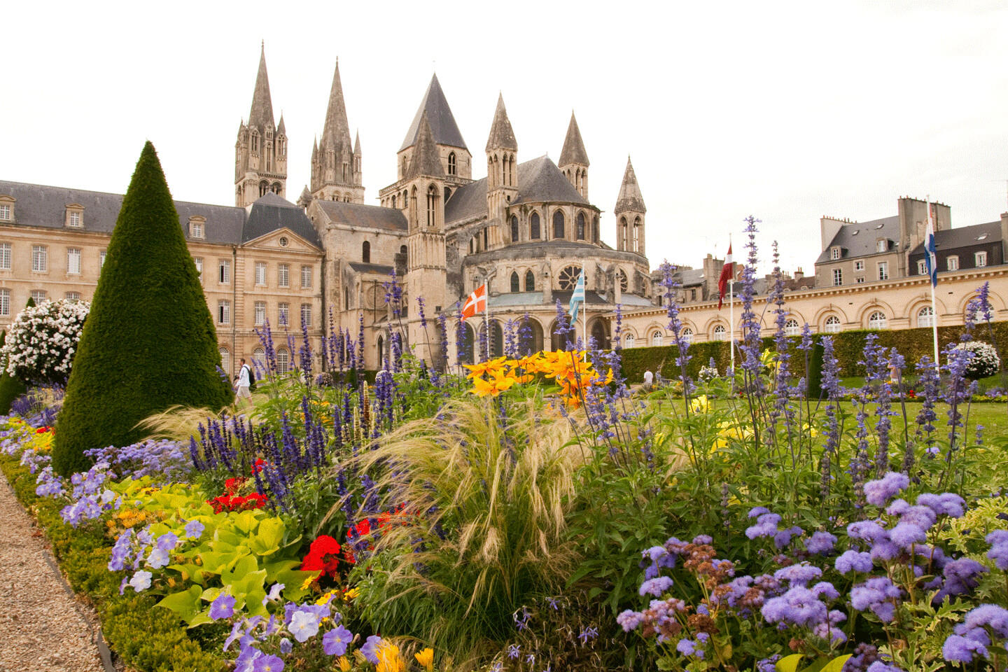 View of the flower garden and the Abbaye aux Hommes in Caen, with historical architecture in the background and a colorful flower bed in the foreground.