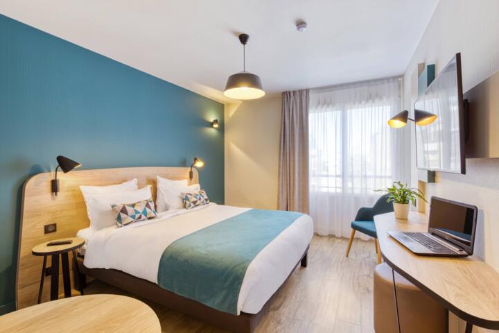 Habitación moderna y luminosa en el Appart’hôtel Appart’City Paris Mairie Clichy, con una cama grande, escritorio, decoración elegante y ventanas con vistas al exterior.