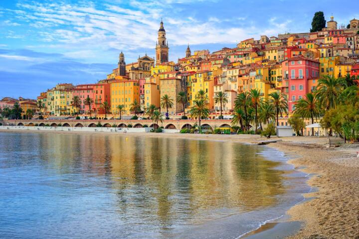 Malerischer Blick auf die Küstenstadt Nizza mit bunten Gebäuden, Palmen und einem Kieselstrand im Vordergrund