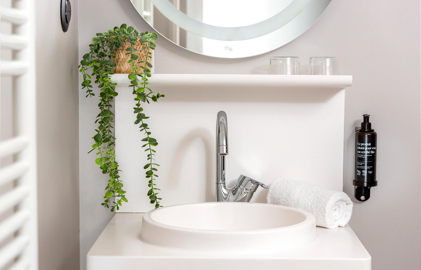Salle de bain propre et soignée avec lavabo, serviette roulée et plante décorative – Appart’hôtel Appart’City